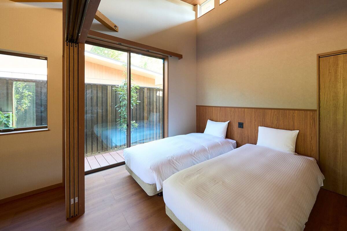 Une chambre d’hôtel avec deux lits, une tête de lit en bois, une porte-fenêtre coulissante donnant sur un balcon et un plancher en bois.