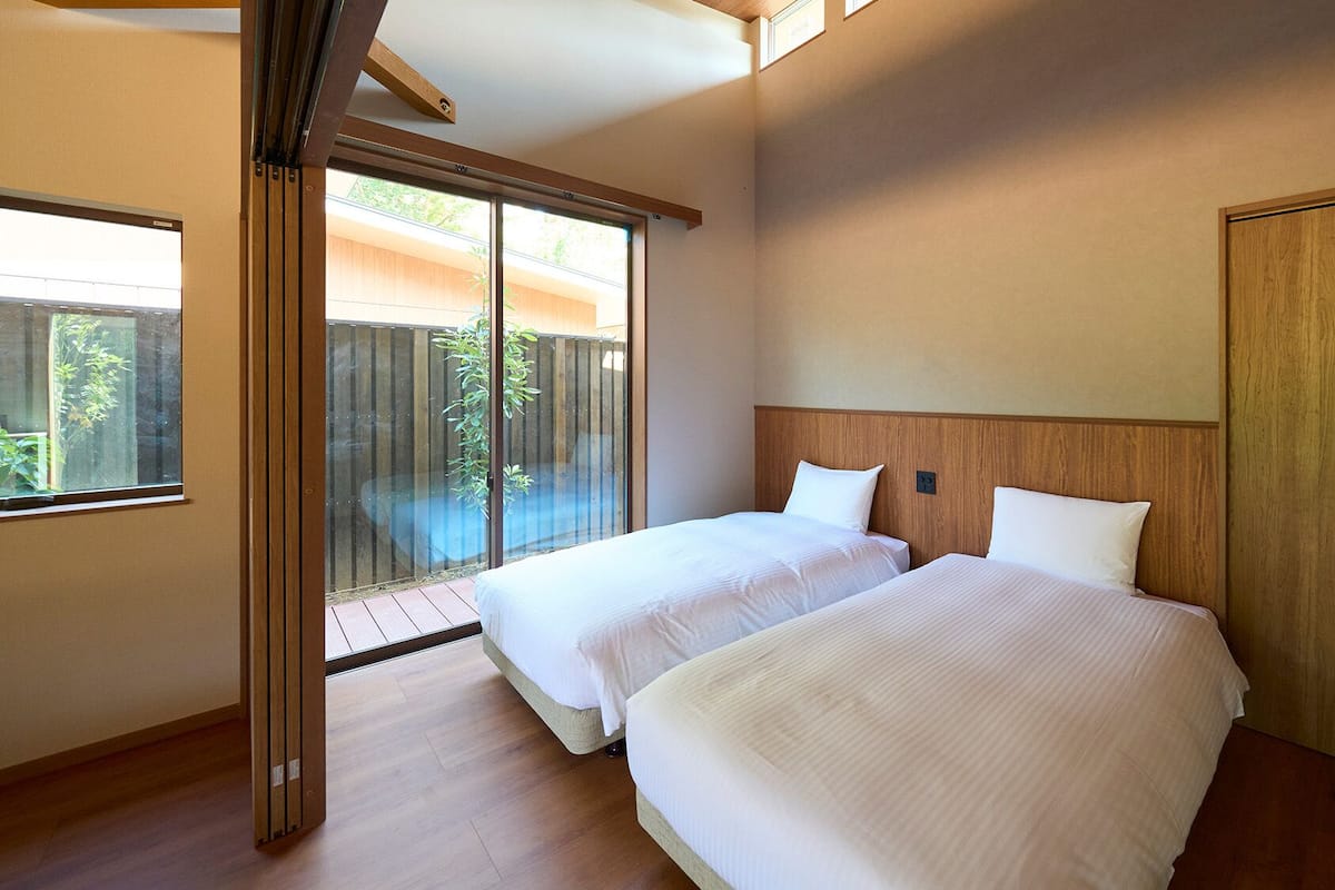 A hotel room with two beds, a wooden headboard, a sliding glass door to a balcony, and a wooden floor.