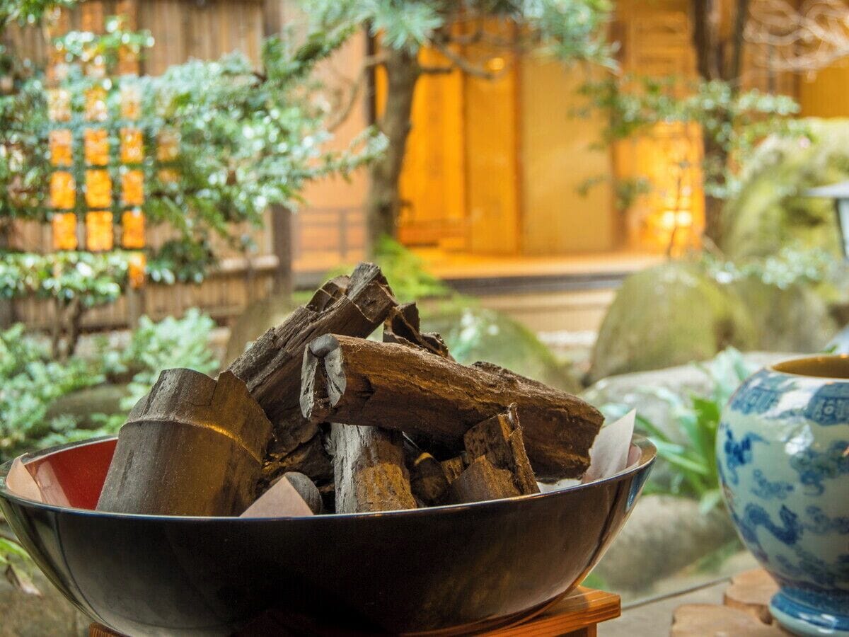 A bowl of firewood on a table with a blue and white ceramic vase in the background.
