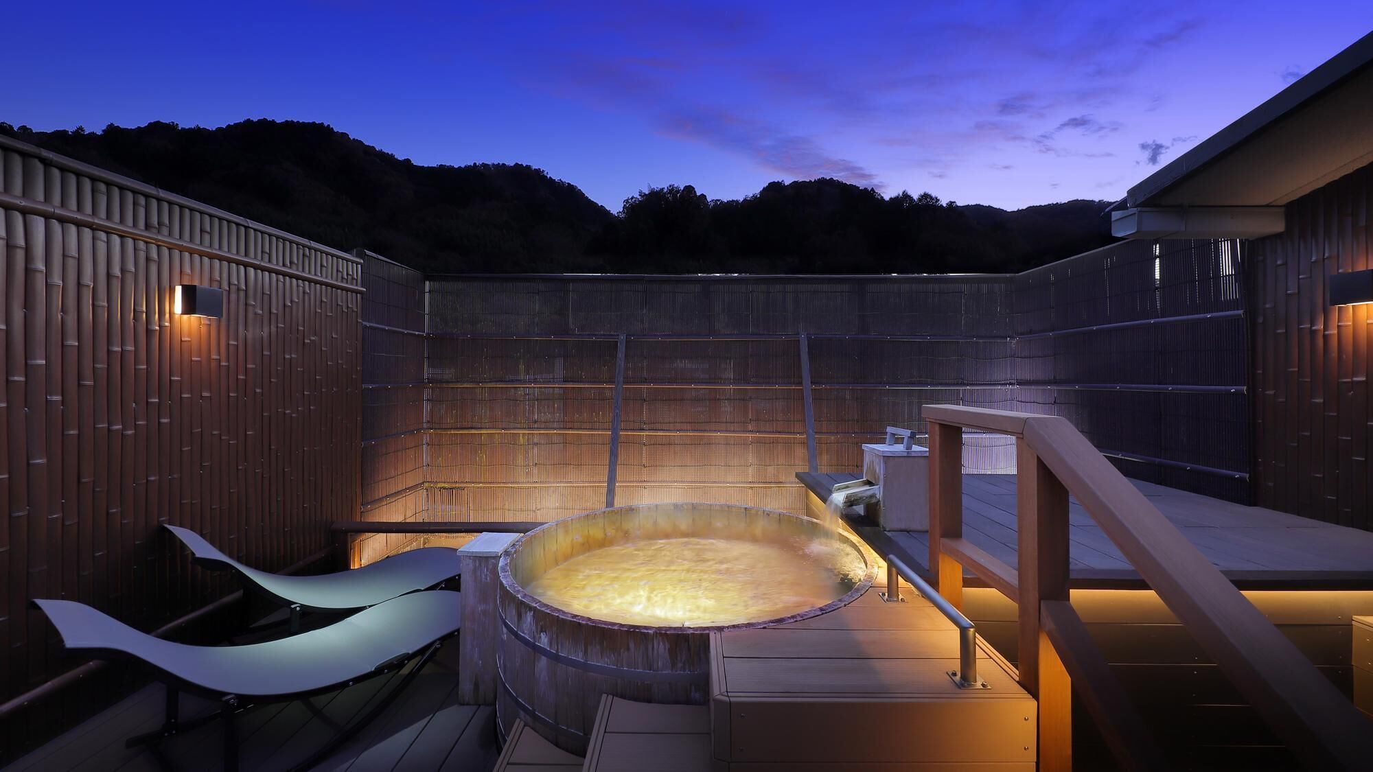 A hot tub in a wooden outdoor setting with a view of hills.