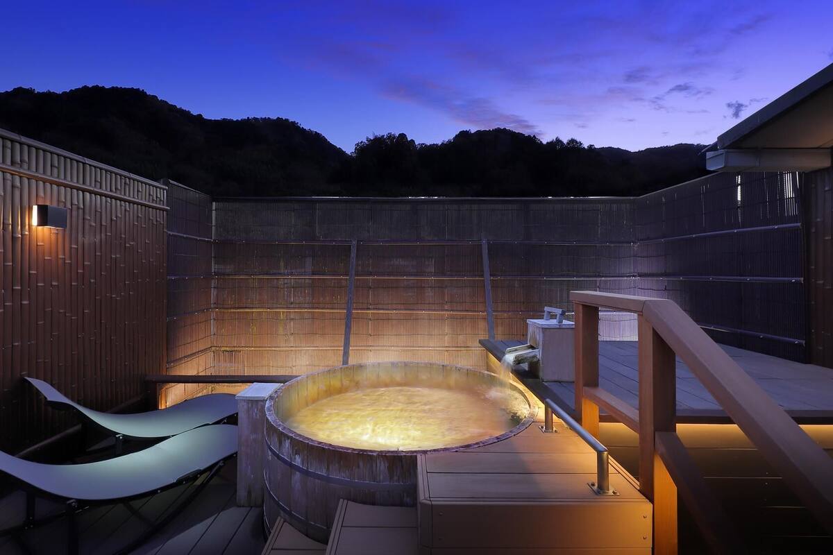 Un jacuzzi en un entorno de madera al aire libre con vistas a colinas.