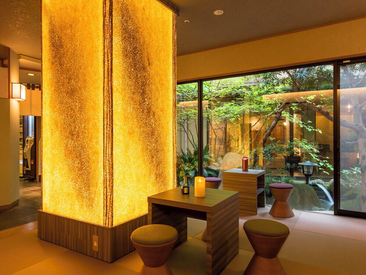 A modern interior with a large illuminated column, a wooden table, and a view of greenery outside.