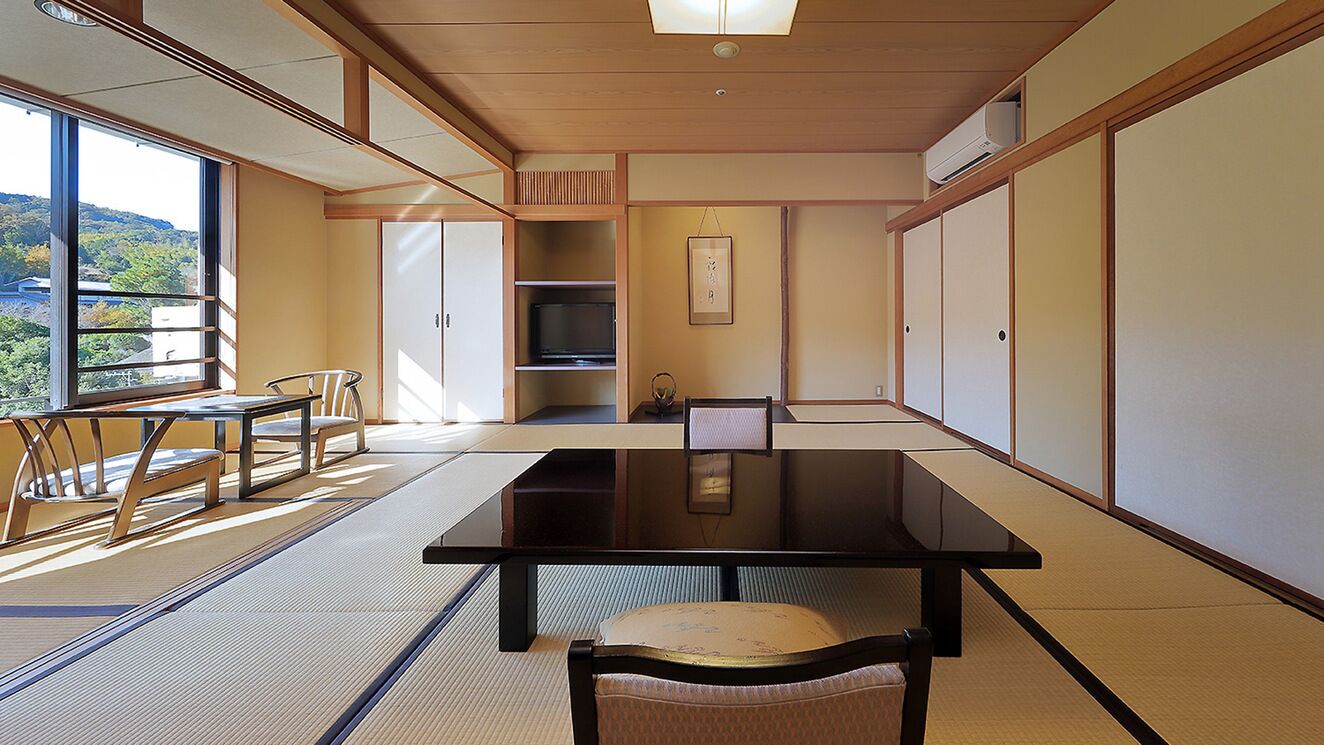 A tatami mat room with a low table, chairs, a television, and sliding doors.