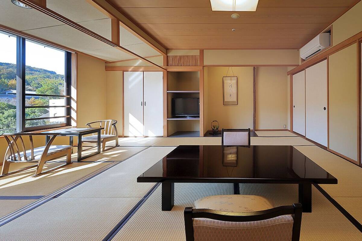 Una habitación con tatamis, una mesa baja, sillas, un televisor y puertas correderas.