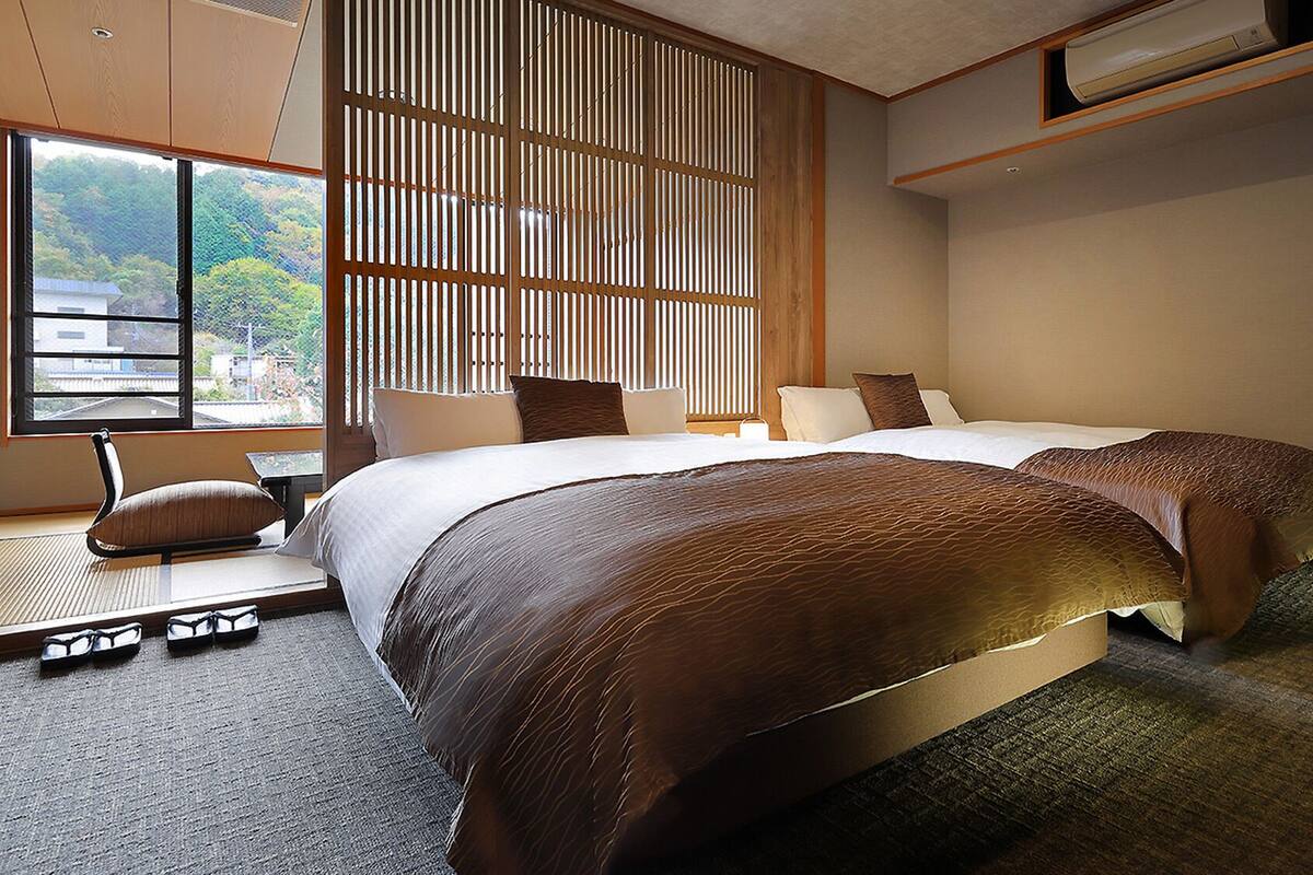 Habitación de hotel con cama, una silla, un ventanal y vistas al verdor exterior.