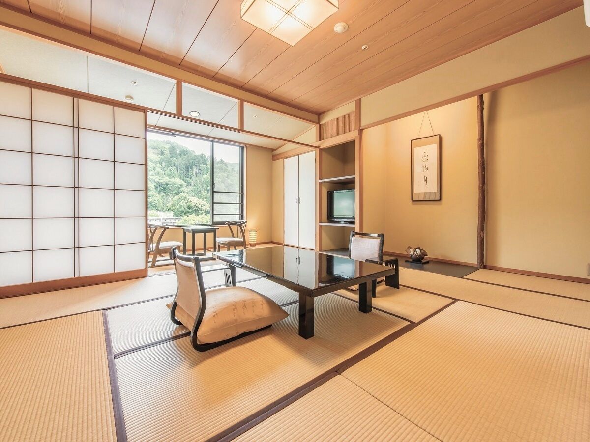 A tatami mat room with a low table, cushions, a TV, and sliding doors.