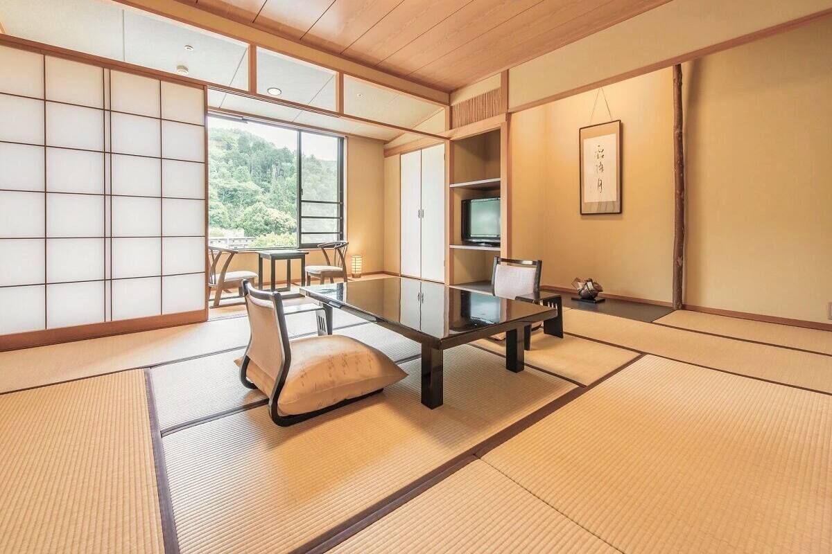 Una habitación con suelo de tatami, una mesa baja, cojines, un televisor y puertas correderas.