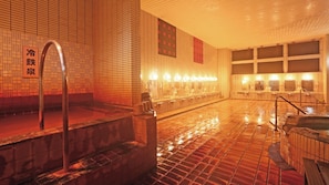 Ein traditionelles japanisches Onsen mit gefliestem Boden, einem Thermalbad und einer Sitzgruppe aus Stein.
