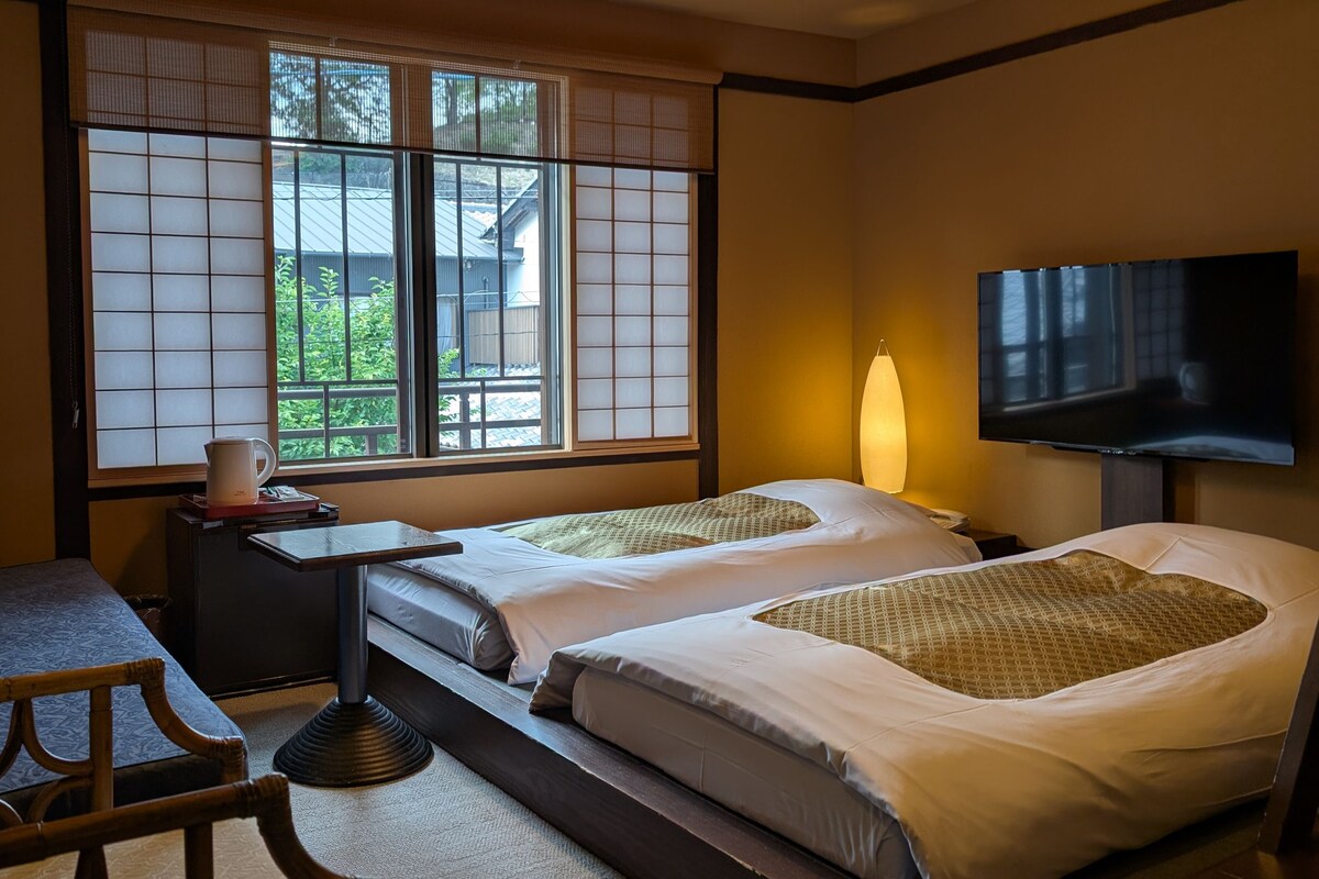 Habitación de hotel con dos camas, un sofá, un televisor y una ventana con vistas a zonas verdes.
