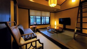 Una habitación de estilo japonés tradicional, con suelo de tatami, una mesa baja, un sofá, un televisor y una escalera.