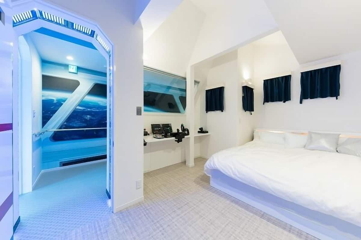 Ein Schlafzimmer mit einem großen Bett, einem Fenster mit Vorhängen, einem Schreibtisch mit Computer und Blick zum Himmel.