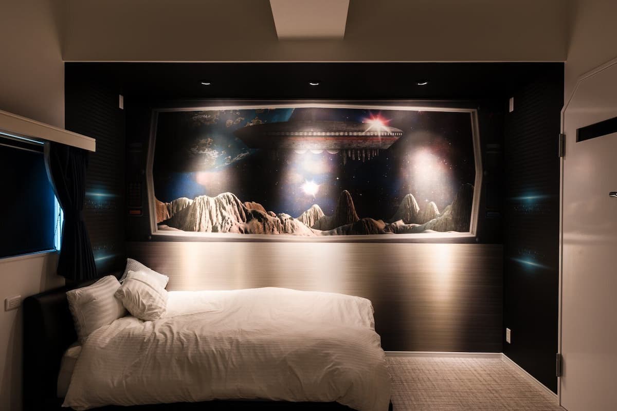 A bedroom with a large bed, a wall-mounted TV, and a mural of a mountainous landscape.