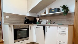 A modern kitchen with a built-in oven, a dishwasher, and a countertop with a coffee maker, kettle, and tea set.