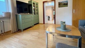A room with a wooden ceiling, a green cabinet, a TV, a dining table with a decorative item, and a door leading to another room.