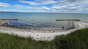 En strand med en person som fiskar, stilla vatten och en klar himmel.