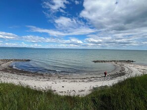 Ein Strand mit einer Person beim Angeln, ruhigem Wasser und blauem Himmel.