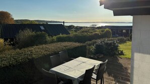 En uteplats med ett bord och stolar, med utsikt över en sjö eller ett annat vattendrag och kullar.