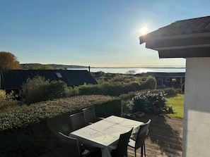 Eine Terrasse mit Tisch und Stühlen, mit Blick auf ein Gewässer und Hügel.