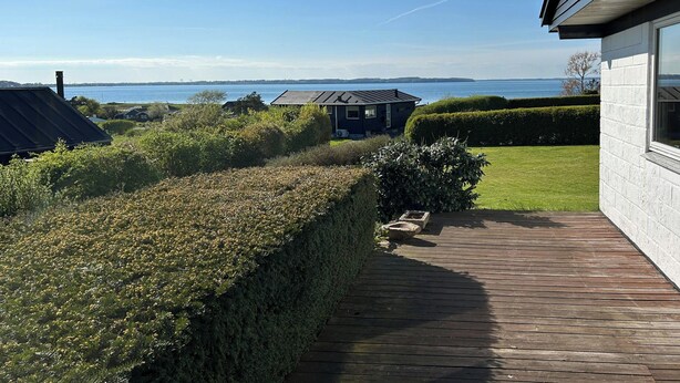 En bostadsfastighet med en träaltan, en välskött gräsmatta och utsikt över havet.