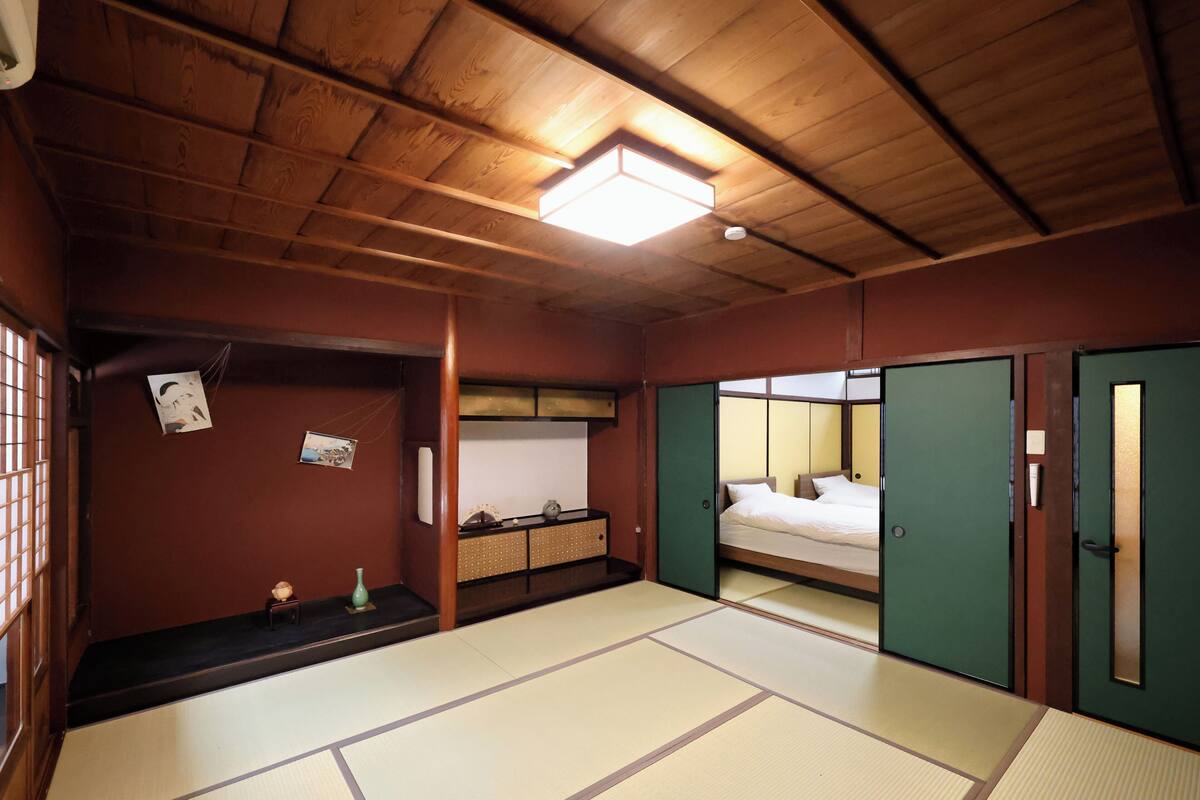 A traditional Japanese room with tatami flooring, a bed, a small table with a vase, and a shelf with a picture frame.
