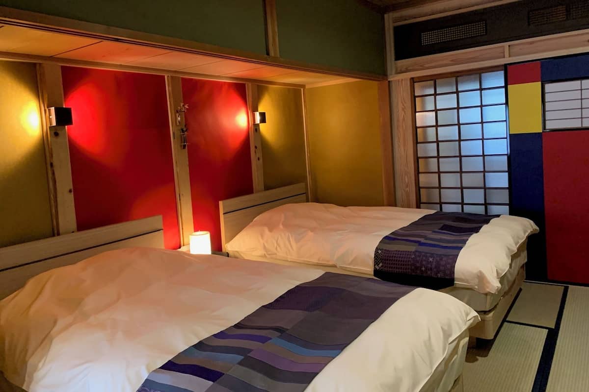 A room with two beds, a window with a grid pattern, and a wall with a colorful panel.