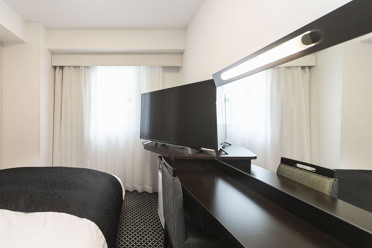 Ein Hotelzimmer mit Bett, Schreibtisch, Flachbildfernseher, Spiegel und einem Fenster mit Vorhängen.