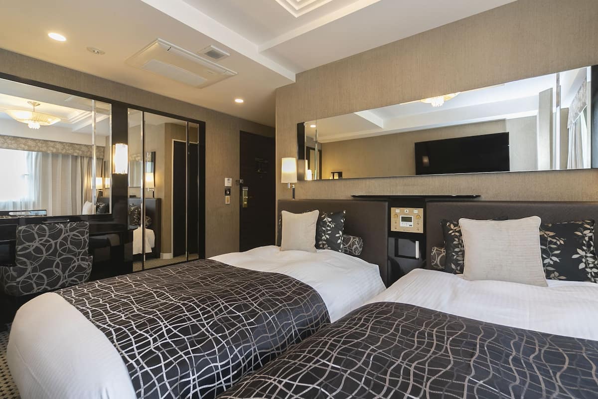 Ein Hotelzimmer mit zwei Betten, einem Schreibtisch, einem Spiegel und einem Fernseher.