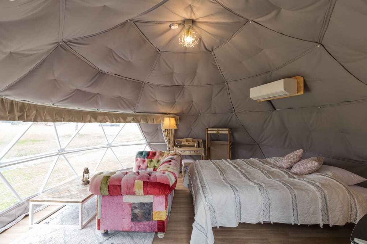 Ein geräumiges Zelt mit einem Bett, einem kleinen Tisch und einer Lampe.