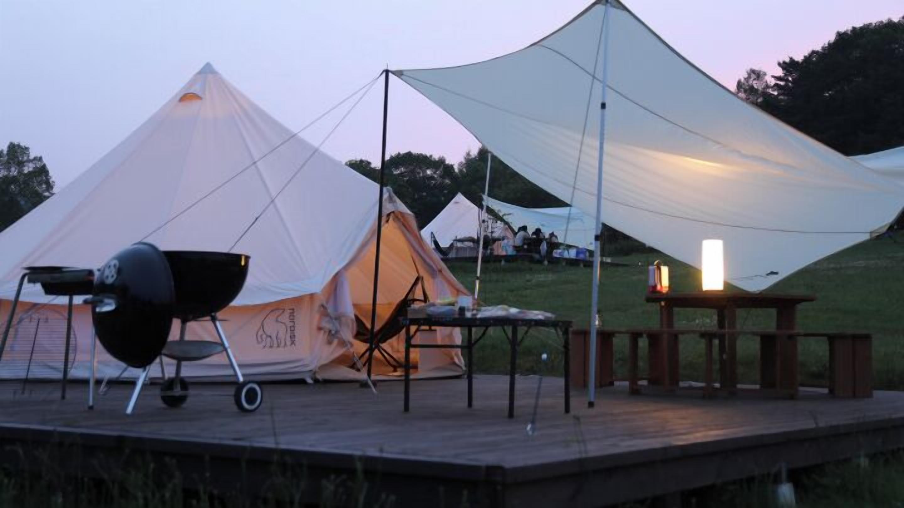 A tent with a grill, a table with a candle, and a wooden deck.