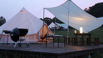 A tent with a grill, a table with a candle, and a wooden deck.