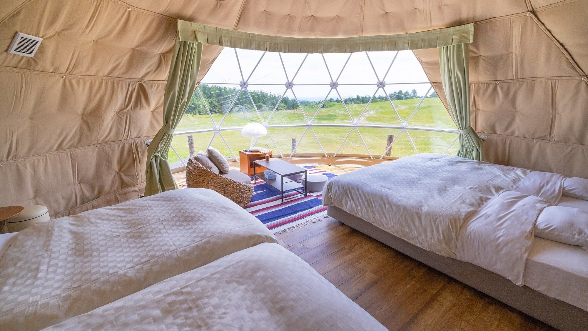 Una carpa con dos camas, una mesa y vistas a un paisaje verde.