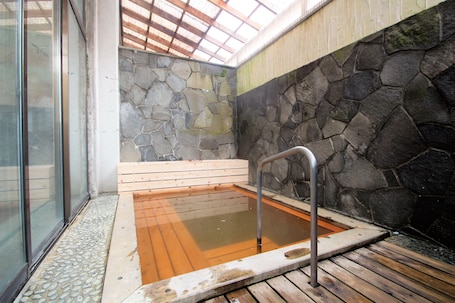 A stone-walled hot tub with wooden steps and a metal handrail.