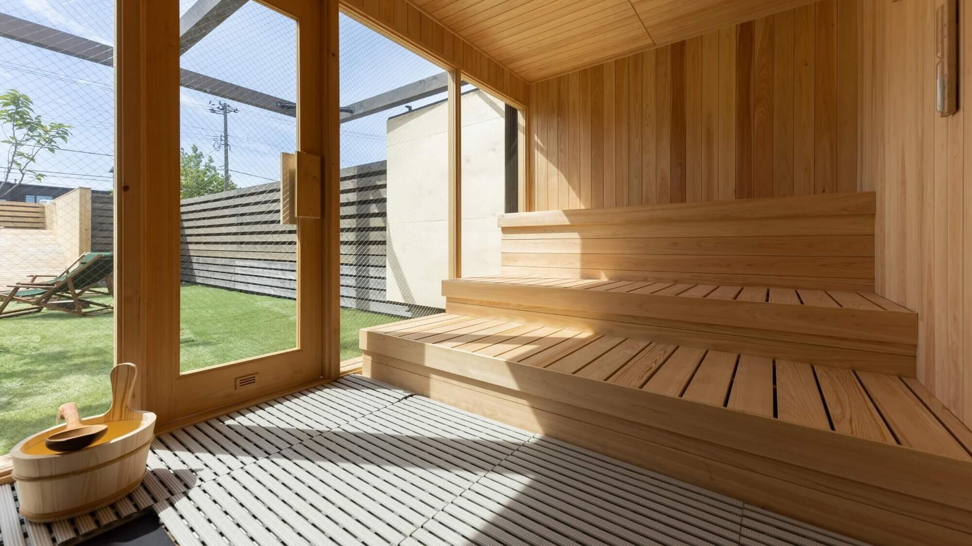 A sauna with wooden benches and a tiled floor, large windows, and a view of a backyard.
