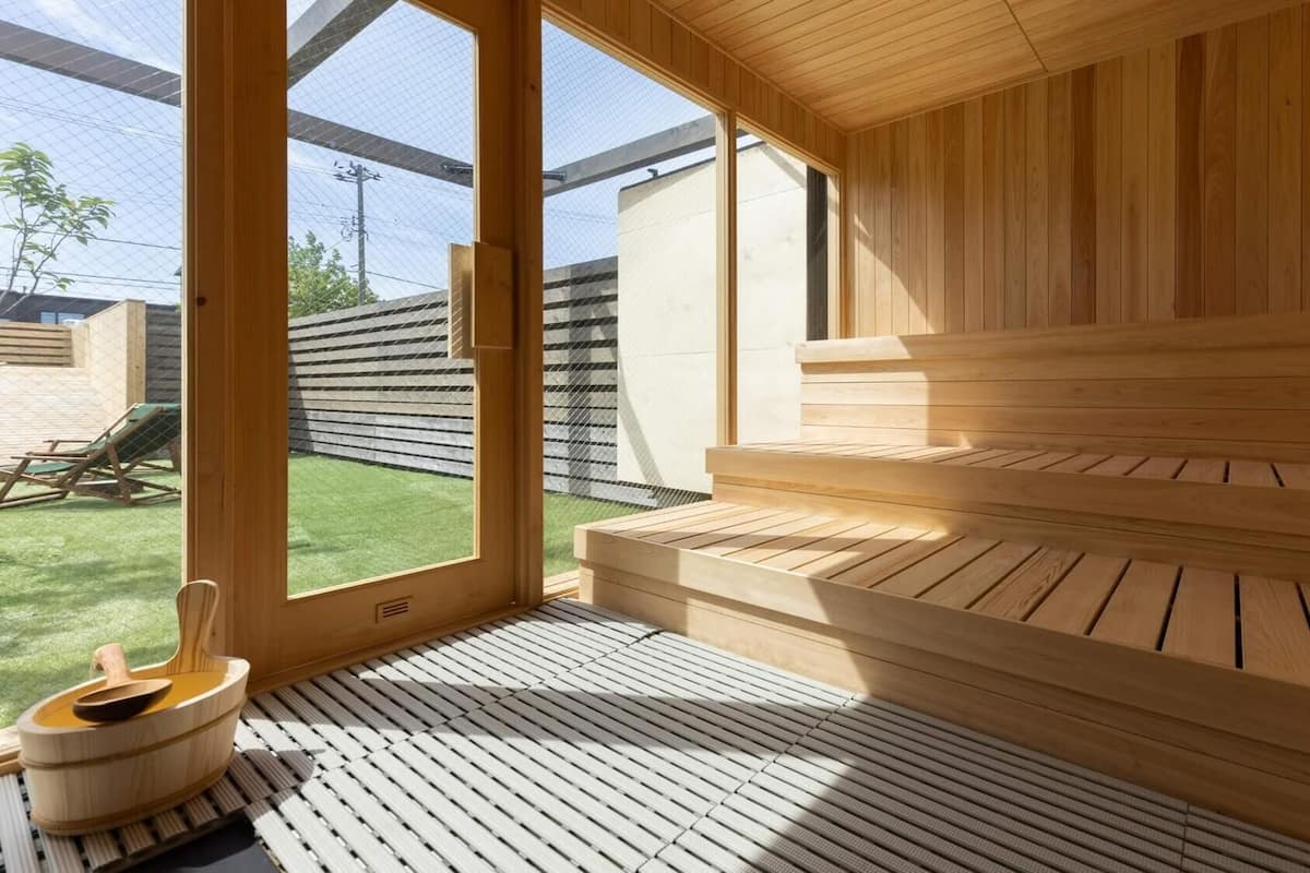 Eine Sauna mit Holzbänken und Fliesenboden, großen Fenstern und Blick auf einen Garten.