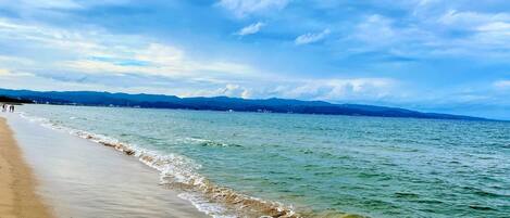 A beach with waves, a clear sky, and distant mountains.