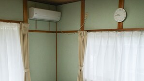 Una habitación con dos camas, una mesita redonda, un reloj de pared y un equipo de aire acondicionado.
