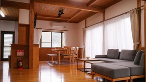 Una habitación con piso de madera, un sofá gris, una mesa de comedor con sillas y una ventana con cortinas.