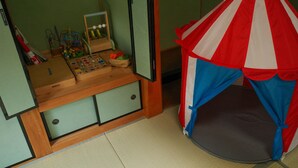 Una habitación con una zona de juegos que incluye una pequeña mesa con juguetes, un coche de juguete y una cesta. Hay una estructura tipo tienda con rayas rojas y blancas.