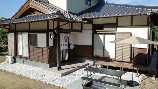 Una casa tradicional japonesa con techo de tejas, vigas de madera y un pequeño espacio al aire libre con mesa y banco.