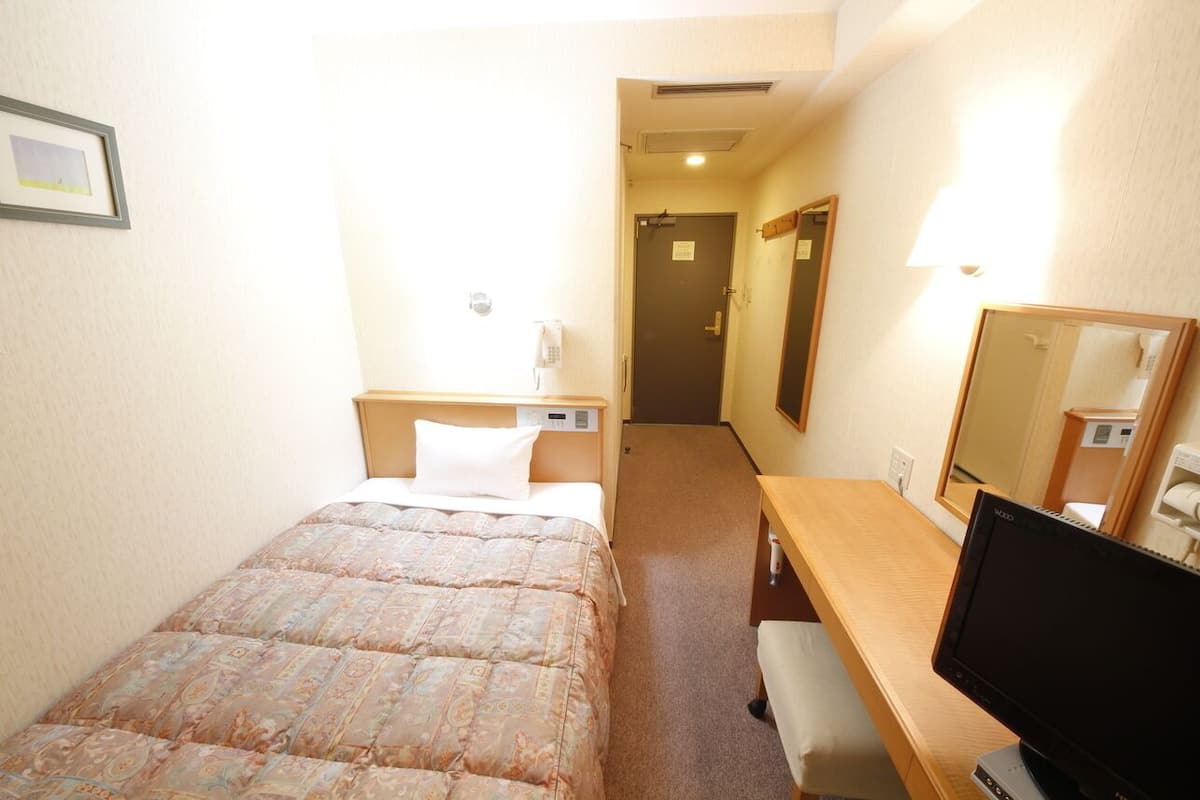 Habitación de hotel con cama, escritorio, televisión, espejo y puerta que da a otra habitación.