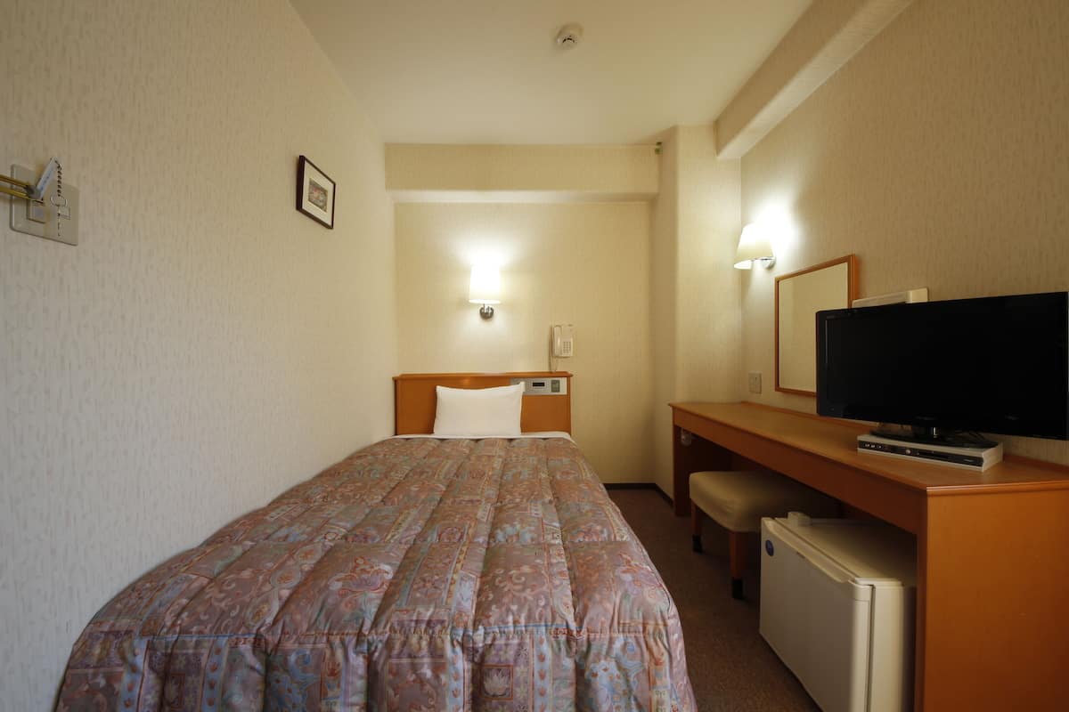 Habitación de hotel con cama, escritorio con televisor, refrigerador pequeño y teléfono en la pared.