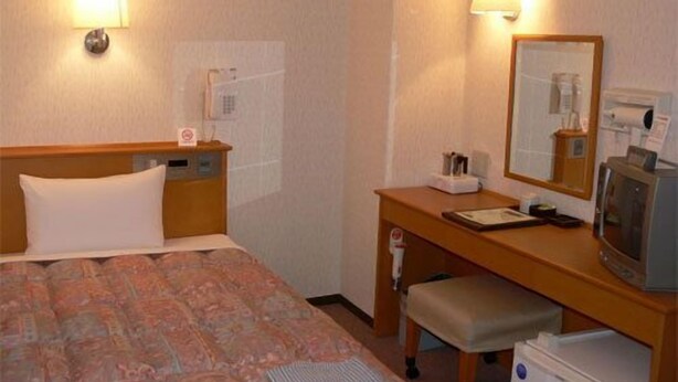 A hotel room with a bed, a desk with a mirror, a telephone, and a television. - Business Inn Kabutan (Fukuyama)