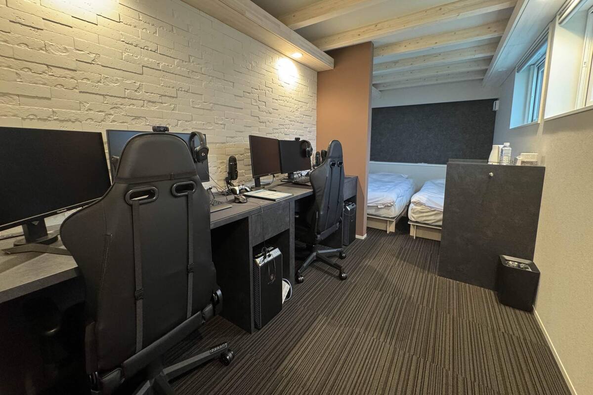 A hotel room with a brick wall, two beds, a desk with computers, and a window.