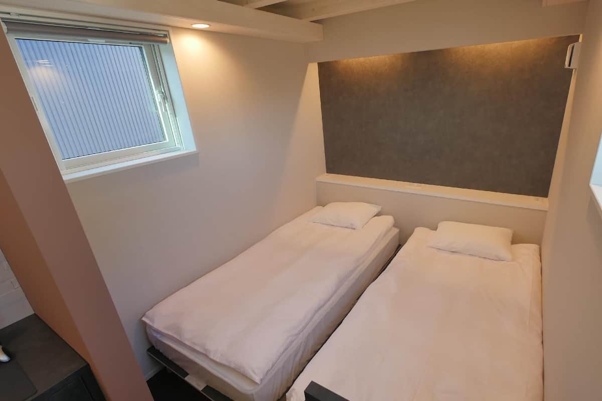 A small, single-room accommodation with two beds, a window, and a built-in bench.