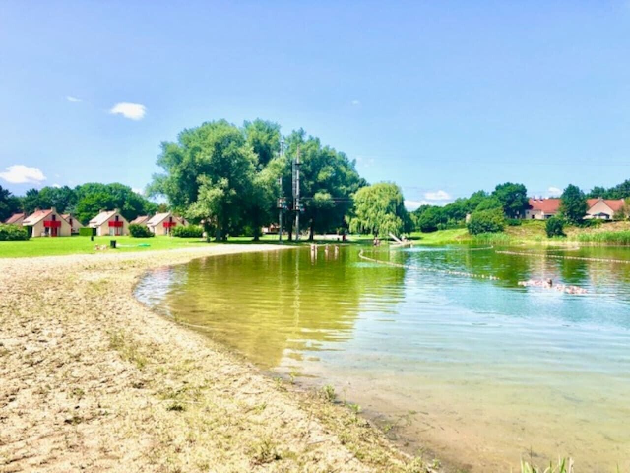 Un lac aux rives sablonneuses, entouré de verdure et de maisons.