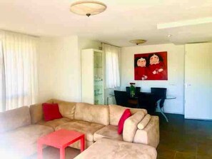 Ein Wohnzimmer mit einem beigefarbenen Sofa, einem roten Tisch und einem Essbereich mit einem schwarzen Tisch und Stühlen.