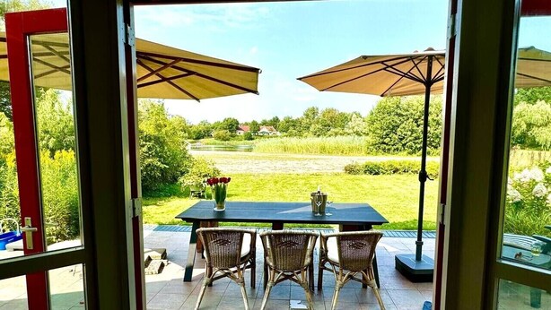 Un patio con tavolo e sedie, un vaso con fiori e ombrelloni.
