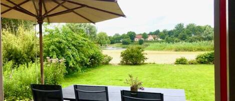 Une terrasse extérieure avec une table et des chaises, un grand parasol et une vue sur un paysage verdoyant.