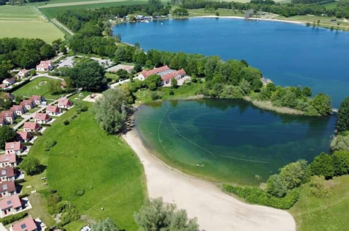 Ovenfra set et søområde omgivet af parcelhuse, med en tydelig kystlinje og et sandet område.