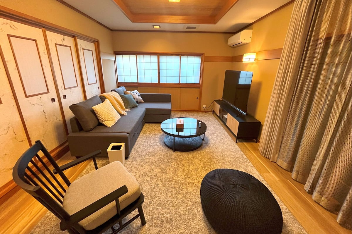 A living room with a sofa, a chair, a coffee table, a television, and a window with curtains.